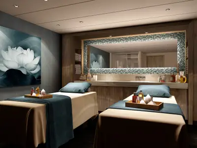 Der luxuriöse Behandlungsraum im Mandara Spa der Norwegian Encore mit zwei Massageliegen und Wellness-Produkten. Ein großes Lotus-Wandbild ziert die Wand.