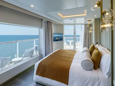Eine modern und luxuriös eingerichtete Suite an Bord der Norwegian Encore mit einem großen Bett, Balkon und Blick auf das weite Meer.