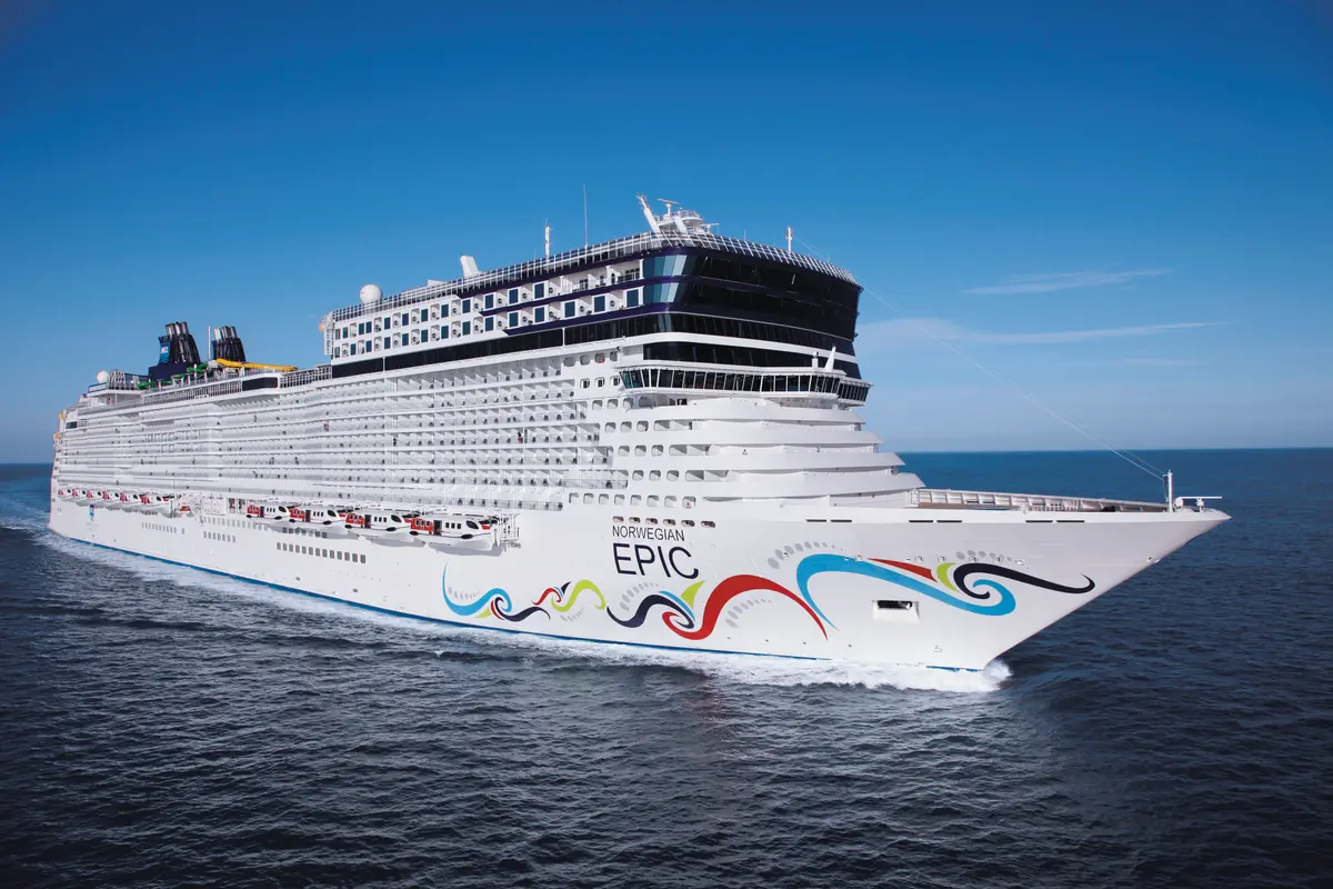Die Norwegian Epic, ein majestätisches Kreuzfahrtschiff, fährt auf tiefblauem Meer unter strahlendem Sonnenschein. Die bunte Bugbemalung und die weisse Bugwelle sind klar sichtbar.