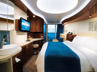 Moderne Balkonkabine der Norwegian Epic. Grosses Bett, Schreibtisch mit TV und Balkon mit Meerblick. Links ein Waschtisch mit blauen Fliesen und Spiegelschrank.