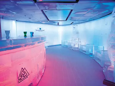 Die Svedka Ice Bar an Bord der Norwegian Epic, komplett aus Eis gefertigt und in Pink und Blau beleuchtet. Man sieht eine Eistheke, Eisgläser und Eisskulpturen.