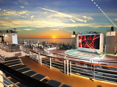 Sonnenuntergang auf dem Oberdeck der Norwegian Epic. Ein grosser LED-Bildschirm mit abstrakten roten Mustern. Davor eine Pool-Bühne, umgeben von Liegestühlen auf mehreren Ebenen.