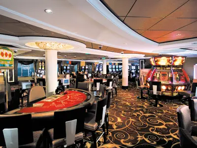 Ein weitläufiges Casino an Bord der Norwegian Epic mit zahlreichen beleuchteten Spielautomaten, Kartentischen und eleganten Sitzgelegenheiten. Im Hintergrund ist das Meer durch Fenster sichtbar.