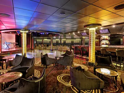 Eine lebhafte Ultra Lounge an Bord der Norwegian Epic bei Abendstimmung, mit einer Bühne, einer Bar, bequemen Lounge-Sesseln und einer Tanzfläche, beleuchtet von farbigen Lichtern.