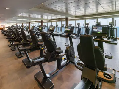 Modernes Fitnesscenter der Norwegian Epic mit Liegeergometern und Laufbändern. Große Fenster bieten weiten Blick auf das Meer. Hell, sauber, ohne Personen.