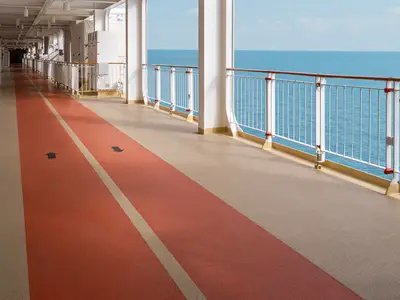Ein roter Joggingpfad mit Richtungspfeilen auf dem Außendeck der Norwegian Epic. Rechts weiße Geländer und das weite, blaue Meer unter klarem Himmel.
