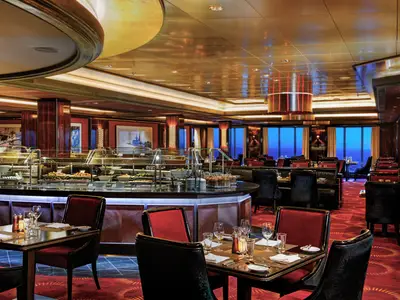 Buffetrestaurant der Norwegian Epic. Gedeckte Tische, Speisenbuffet. Fenster mit Meerblick bei Dämmerung. Dunkles Holz, warme Lichter, luxuriöse Atmosphäre.