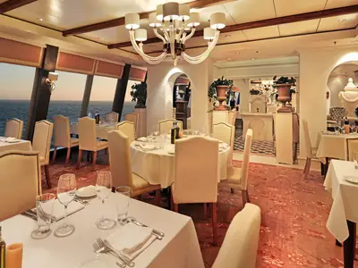 Ein elegantes Restaurant an Bord der Norwegian Epic mit Tischen, Stühlen und einem weiten Blick auf das Meer bei Sonnenuntergang.