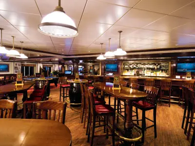 O'Sheehan's Bar & Grill an Bord der Norwegian Epic. Holztische, Barhocker, beleuchtete Bar, Flachbildschirme, Billardtisch. Warme, einladende Atmosphäre.
