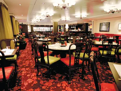 Ein asiatisches Spezialitätenrestaurant an Bord der Norwegian Epic. Roter Teppich mit Blüten, dunkle Holzstühle, runde Tische. Offene Küche im Hintergrund.