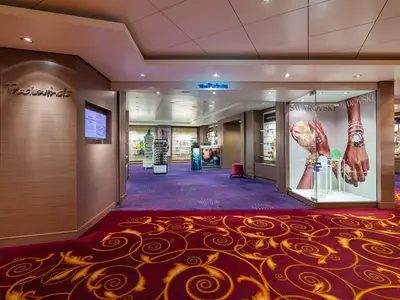 Der helle und moderne Shop 'The Pointe' an Bord der Norwegian Epic. Vitrinen mit Uhren und Swarovski-Schmuck, lila Teppichboden. Roter Teppich mit Mustern führt zum Eingang.