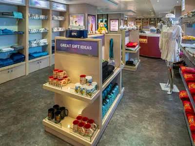 Der moderne Shop an Bord der Norwegian Epic zeigt Regale mit Kleidung, Tassen und Souvenirs. Eine silberne Schaufensterpuppe praesentiert ein Sommerkleid; Verkaufstheke im Hintergrund.