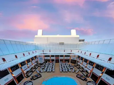 Blick auf den The Haven Courtyard der Norwegian Epic. Das Deck ist mit Liegen und Sitzbereichen ausgestattet. Darüber ist ein Himmel mit rosa und blauen Wolken im Sonnenuntergang zu sehen.