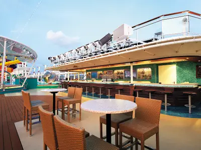 Ein Blick auf die Waves Bar auf Deck 15 der Norwegian Epic. Die Bar mit blauen Mosaikfliesen bietet Hocker und Tische, im Hintergrund sind der Pool und Wasserrutschen zu sehen.