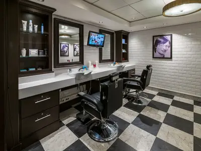 Barbershop an Bord der Norwegian Epic mit zwei schwarzen Friseurstühlen, Waschbecken, weißen Kachelwänden und Schachbrettmusterboden.