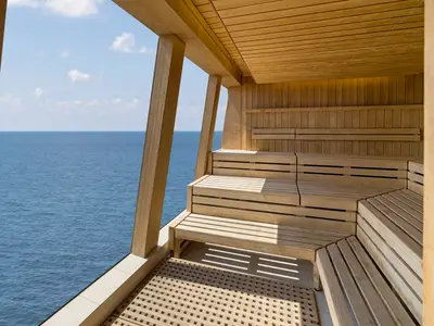 Eine helle Holzsauna mit gestuften Bänken und einem weiten Blick auf das offene Meer unter blauem Himmel an Bord der Norwegian Epic.