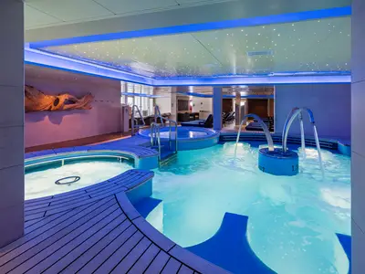 Das Spa-Thermalbad an Bord der Norwegian Epic. Türkisfarbene Pools mit Sprudel und Wasserfällen, umgeben von Holzdecks. Blaue LED-Beleuchtung und Sternenhimmel-Decke für Entspannung.
