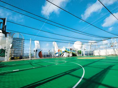 Ein Basketballfeld und Sportbereich mit zwei Körben und Fangnetzen unter klarem Himmel an Bord der Norwegian Epic, umgeben von Schiffsaufbauten.