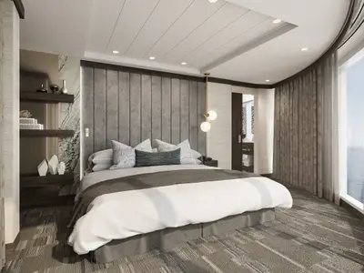 Helles Schlafzimmer der Owners Suite an Bord der Norwegian Epic. Großes Bett, Kopfteil, Nachttischlampen und eine runde Fensterfront mit Meerblick. Moderne Einrichtung in Grau- und Weißtönen.