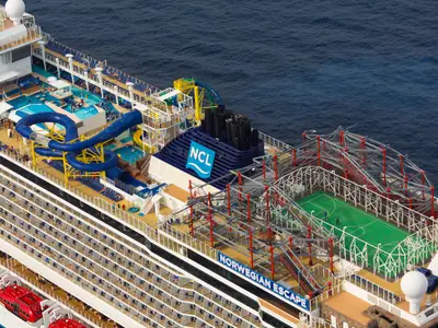 Luftaufnahme der oberen Decks der Norwegian Escape auf dem Meer. Sichtbar sind Wasserrutschen, Pools, ein Sportplatz, ein weitläufiger Kletterpark und zahlreiche Balkonkabinen.