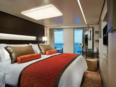 Geräumige Balkonkabine an Bord der Norwegian Escape. Ein grosses Bett mit weisser Bettwäsche und luxuriösen Kissen dominiert den Raum. Durch eine Glastür ist ein Balkon mit Meerblick zu sehen. Moderne Beleuchtungselemente und ein Schminktisch mit beleuchtetem Spiegel ergänzen das elegante Interieur.