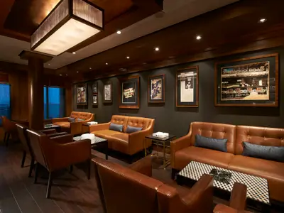 Die luxuriöse Zigarren-Lounge an Bord der Norwegian Escape. Braune Ledersofas und Sessel, dazu dunkle Wände mit gerahmten Bildern und Holzelementen. Eine gediegene, einladende Atmosphäre.