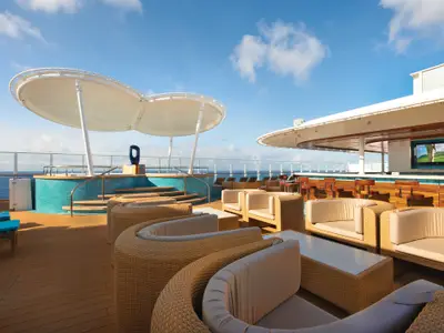 Das sonnige Oberdeck der Norwegian Escape zeigt moderne Rattan-Lounges, einen türkis gefliesten Whirlpool und eine offene Bar. Im Hintergrund ist der weite Ozean zu sehen.