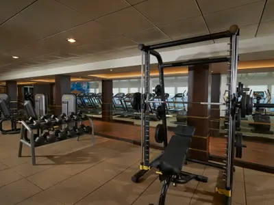 Geräumiges Fitnesscenter an Bord der Norwegian Escape mit modernen Kraftgeräten, Hanteln und Laufbändern. Große Fenster bieten einen weiten Blick auf das Meer während des Trainings.