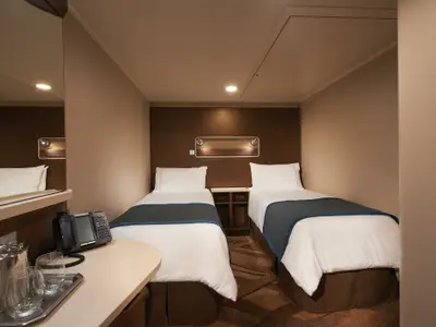 Eine stilvolle Innenkabine an Bord der Norwegian Escape mit zwei getrennten Betten und einem Schreibtisch. Die Kabine ist in warmen Brauntönen gehalten und gut beleuchtet.