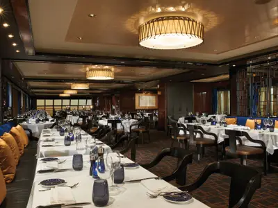 Blick in das elegante Cagney's Steakhouse auf der Norwegian Escape mit weiß gedeckten Tischen und bequemen Sitzgelegenheiten, bereit für den Service.