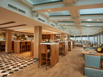Das stilvolle "Food Republic" Restaurant an Bord der Norwegian Escape. Zahlreiche Tische und Barhocker mit Tablets, moderne Holzeinrichtung und große Fenster mit Meerblick.