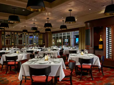 Elegantes Restaurant Le Bistro an Bord der Norwegian Escape mit vielen Tischen, roten Stühlen, dunklen Wänden mit Spiegeln und einem großen Weinregal.