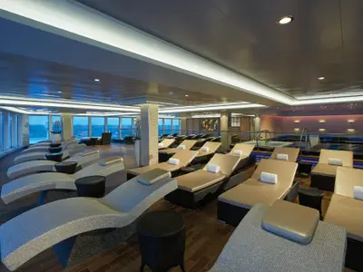 Ein moderner Spa-Bereich mit zahlreichen beigen Liegen, Thermalbecken und großen Fenstern zum Meer an Bord der Norwegian Escape.