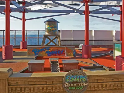 Ansicht des Minigolfplatzes "Birdie Bogey" auf dem Oberdeck der Norwegian Escape. Bunte Bahnen mit einer Wasserturm-Attrappe und dem Meer im Hintergrund.