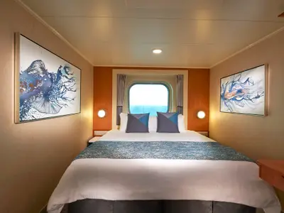 Gemütliche Aussenkabine an Bord der Norwegian Gem mit Doppelbett, Meerblick-Fenster und zwei abstrakten, blauen Wandbildern.