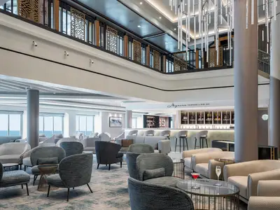 Die Magnums Champagne & Wine Bar der Norwegian Gem. Ein eleganter, zweistoeckiger Loungebereich mit Bar, Meerblick, Sitzgruppen, moderner Beleuchtung und dekorativen Balustraden.