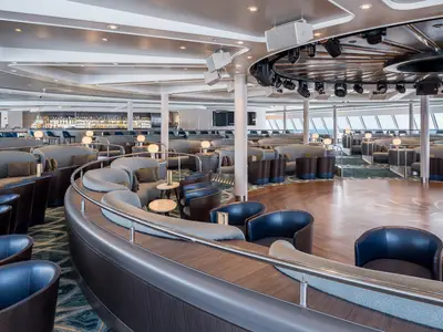 Die helle Spinnaker Lounge an Bord der Norwegian Gem zeigt stilvolle Sitzbereiche, eine gut sortierte Bar und eine Tanzfläche. Große Panoramafenster bieten einen weiten Blick auf das offene Meer.