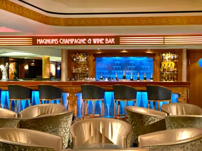 Innenansicht der Magnums Champagne & Wine Bar an Bord der Norwegian Gem. Elegante Bar mit blauer Beleuchtung, Champagnerflaschen und Gläsern, sowie gemütlichen Sesseln im Vordergrund.