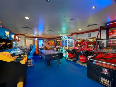 Eine lebhafte Videospielhalle an Bord der Norwegian Gem mit einer Vielzahl von Spielautomaten, darunter Rennsimulatoren, ein Airhockey-Tisch und ein Basketball-Wurfspiel, alle auf einem blauen Teppichboden.