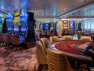Ein weitläufiges Casino an Bord der Norwegian Gem, beleuchtet mit blauen LED-Lichtern. Reihen von Slot-Maschinen säumen die Wände, während im Vordergrund mehrere Pokertische mit roten Filzflächen und bequemen Stühlen zu sehen sind. Im Hintergrund ist durch große Fenster das offene Meer sichtbar, was eine entspannte Atmosphäre schafft. Das Casino ist modern eingerichtet und bereit für Spieler.