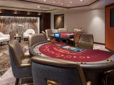 Innenansicht des Casinos an Bord der Norwegian Gem. Es sind Blackjack-Tische mit rotem Filz, Chips und bequemen Ledersesseln zu sehen. Eine elegante Marmorwand im Hintergrund.