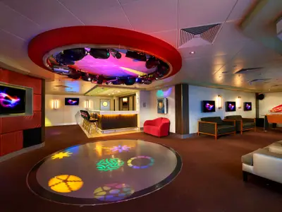 Club- und Barbereich der Norwegian Gem. Runde Tanzfläche mit bunten Lichtprojektionen, Bar, Sitzgelegenheiten, Fernseher, Foosball-Tisch. Moderne Beleuchtung, lebhafte Atmosphäre.