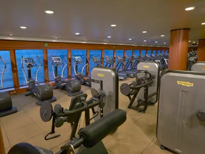 Ein helles Fitnessstudio an Bord der Norwegian Gem. Zahlreiche moderne Technogym-Fitnessgeräte stehen bereit, darunter Laufbänder und Ellipsentrainer mit Blick auf das Meer.