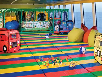 Der lebhafte Tree Tops Kid's Club an Bord der Norwegian Gem mit bunten Klettergerüsten, Spielmatten und Spielzeug wie Bällen, Zügen und Bussen.