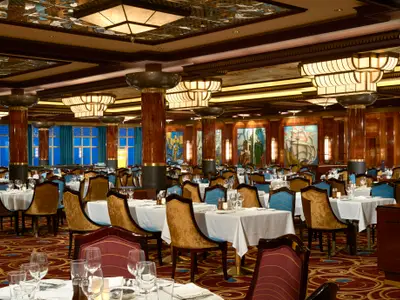 Blick in das geräumige und elegant eingerichtete Grand Pacific Restaurant an Bord der Norwegian Gem mit vielen eingedeckten Tischen, Holzvertäfelung und Art Deco-Stil.