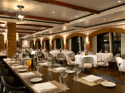 Das Restaurant La Cucina an Bord der Norwegian Gem. Eleganter Innenraum mit Backsteinbögen, Holzbalken und warmem Licht. Zahlreiche Tische sind festlich mit weißen Decken und Gedecken vorbereitet.