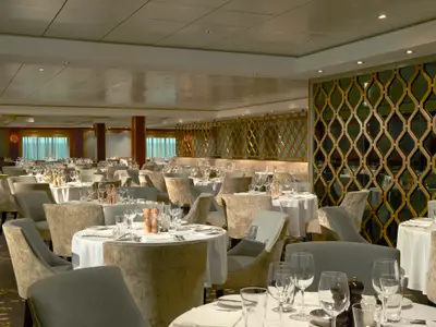 Das elegante Hauptrestaurant Magenta Dining Room an Bord der Norwegian Gem, mit vielen festlich gedeckten Tischen, bequemen Stühlen und stilvollen goldenen Wandelementen.