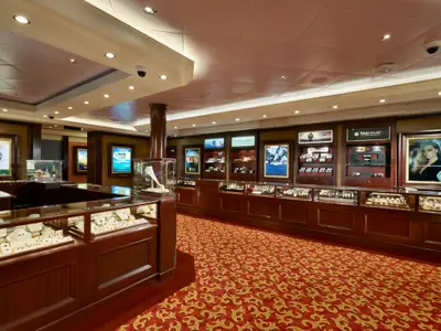Der Juwelier- und Uhrenshop an Bord der Norwegian Gem. Edle Vitrinen zeigen Schmuck und Zeitmesser. Dunkles Holz und roter Teppich schaffen eine luxuriöse Atmosphäre. Keine Personen.