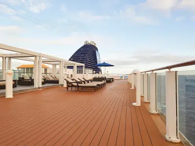Das Sonnendeck der Norwegian Gem mit Liegestühlen und Loungemöbeln unter Pergolen. Blick auf den blauen Schornstein und das Meer.
