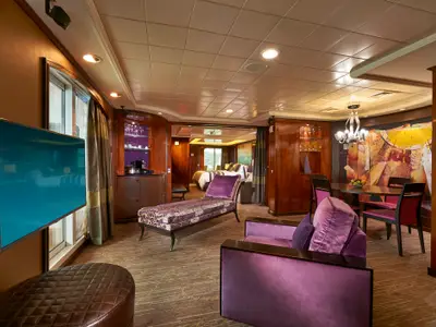 Blick in die luxuriöse Owners Suite an Bord der Norwegian Gem, die einen eleganten Wohnbereich mit lila Möbeln, Essbereich und ein angrenzendes Schlafzimmer mit Blick nach draußen zeigt.